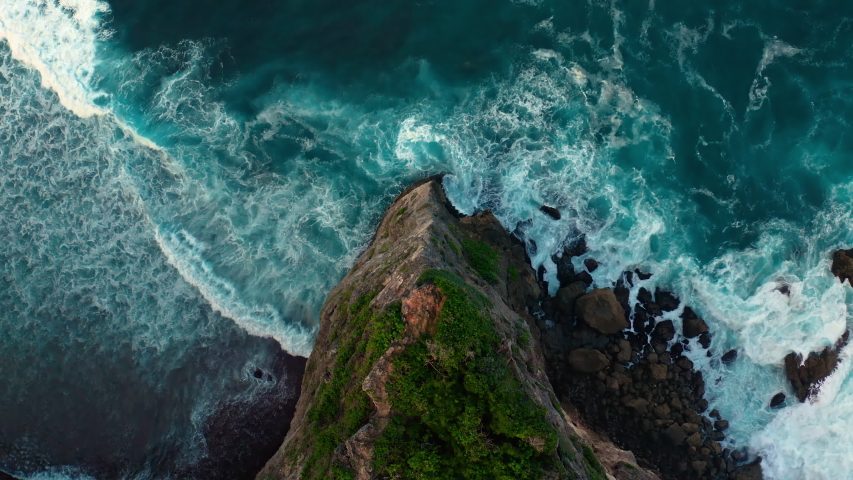 Top down aerial view from above of giant ocean waves crashing and foaming on empty sand tropical beach with big rock stones. Bird's eye aerial shot of golden beach meeting deep blue ocean water. Royalty-Free Stock Footage #1054704032