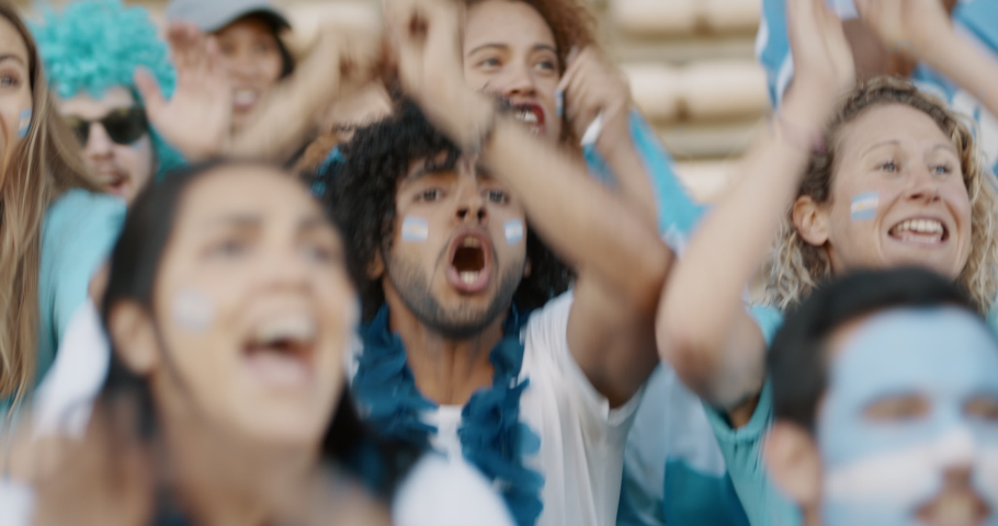 Crowd of soccer fans from Argentina cheering their team with a blue garlands and argentinian flags at stadium. Football fans sitting at stadium starts cheering when their national team scores a goal.
 Royalty-Free Stock Footage #1054708766
