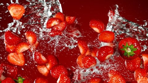 Super Slow Motion Shot of Flying Fresh Strawberries and Water Side Splash on Red Background at 1000fps.