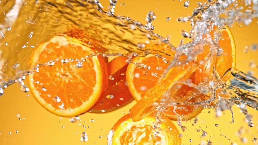 Super Slow Motion Shot of Flying Fresh Orange Slices and Water Side Splash on Orange Background at 1000fps.