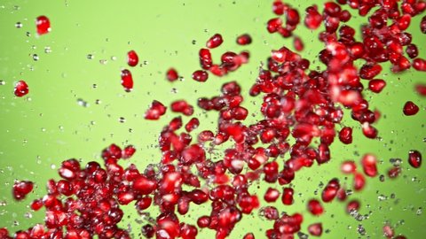 Super Slow Motion Shot of Fresh Pomegranate Seeds and Water Side Collision on Green Background at 1000fps.