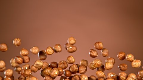 Super Slow Motion Shot of Flying Hazelnuts After Being Exploded on Brown Gradient Background at 1000 fps.