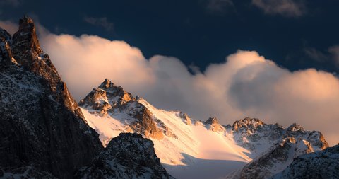 Time lapse of golden sunset over sharp rocky mountains covered with snow