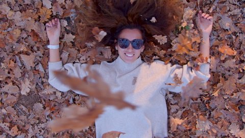 The girl lies on the yellow fallen leaves and leaves fall on her. Autumn concept.