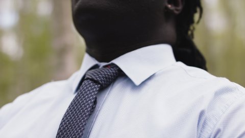 African businessman adjusting necktie in the nature. Close up slow motion shot.