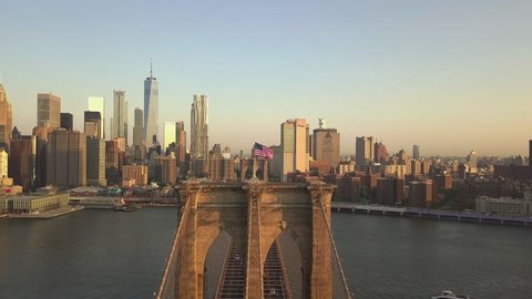 AERIAL: Flight over Brooklyn Bridge with American flag waving and East River view over Manhattan New York City Skyline in beautiful 