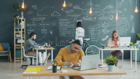 Zoom-in time lapse of Arab man working in shared office writing and typing with laptop while coworkers are moving around talking cooperating. Teamwork and workplace concept. - Powered by Shutterstock - Get 15% off with code: PIKWIZARD15