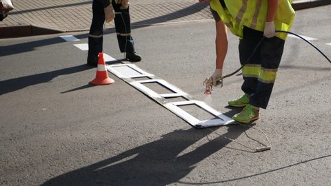 People draw the road. A road worker paints a zebra with a hand tool. Road marking. Workers and paint sprayers for roads. Thermoplastic paint for road marking.