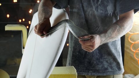 Surfboard manufacturing, Shaper is shaving rails on a surfboard. Concept of small business owner, skilled professional, occupation & job in America. 