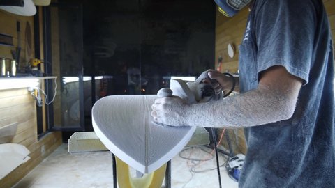 Surfboard manufacturing, Shaper sanding the bottom of the surfboard. Concept of small business owner, skilled professional, occupation & job in America. 