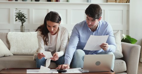 Focused happy family couple holding paper documents, managing utility bills, household payments together at home. Smiling married young man and woman calculating monthly budget, income and outcome.