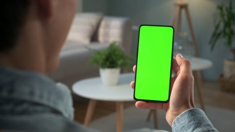 Handheld Camera: Back View of Brunette Man Holding Chroma Key Green Screen Smartphone Watching Content Without Touching or Swiping. Boy Using Mobile Phone, Browsing Internet, Watching Content,