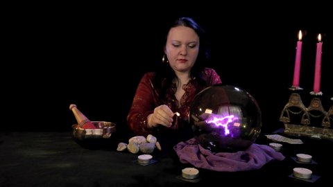 A fortuneteller in a magic salon lights candles on a black background behind magic fire