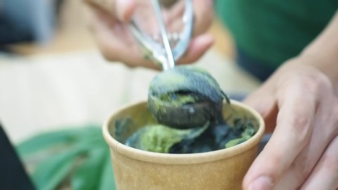 Scooping two tone soft served ice cream, matcha and charcoal from paper container to a bowl. Healthy eating concept, selective focus.  Stock Video