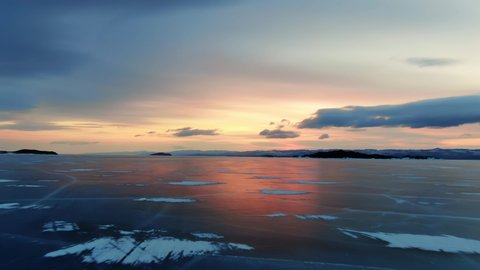 Northern landscape frozen lake drone flying down with beautiful reflection on ice at sunset 4K. Amazing winter Baikal with red sunrise. View drone flight on north frost lake. Natural reflection sunset