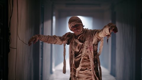 Scary ancient mummy in bandages in haunted house. Guy in thematic halloween costume doing a dance with broken moves of mummy zombie 4k footage