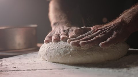Closeup shot of hands of senior bakery chef applying flour on dough, old man kneading dough, making bread using traditional recipe, isolated on black background 4k footage