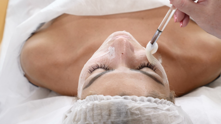 Beauty clinic concept. Young woman getting professional facial procedure. Beautician spreads foam mask on female face with brush. face renovation concept. Top view. 4 k video | Shutterstock HD Video #1054718765