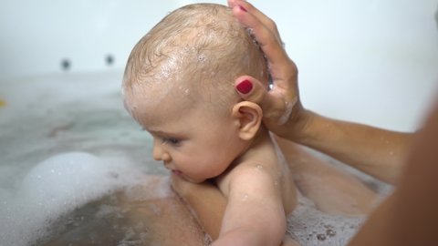 An adorable baby boy taking a bath with mother washing his head 4K