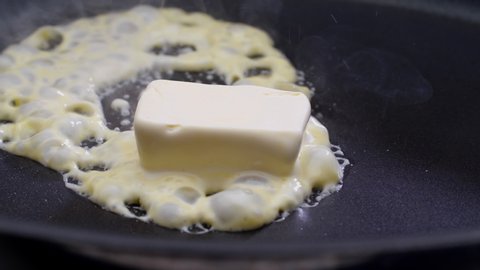 Butter melting sizzling in frying pan on stove. Close up.