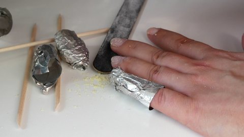 Removal of shellac with nails,a bamboo stick.Makes herself a manicure.Liquid with acetone and aluminum foil.On a white table,closeup shot.Hand care at home.