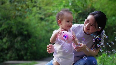 Slow motion of happy little asian baby girl playing soap bubble together with her mother outdoor in the park adorable one year old baby lifestyle footage