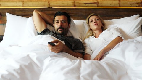 Couple watching television together on bed Husband change to favorite channel wife don't want to watch it and snatch remote control tv from husband, changing her favorite program that make guy angry