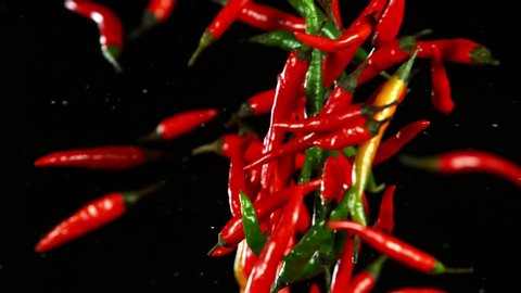 Super slow motion of coloured chilli peppers in collision, black background. Filmed on high speed cinema camera, 1000 fps.