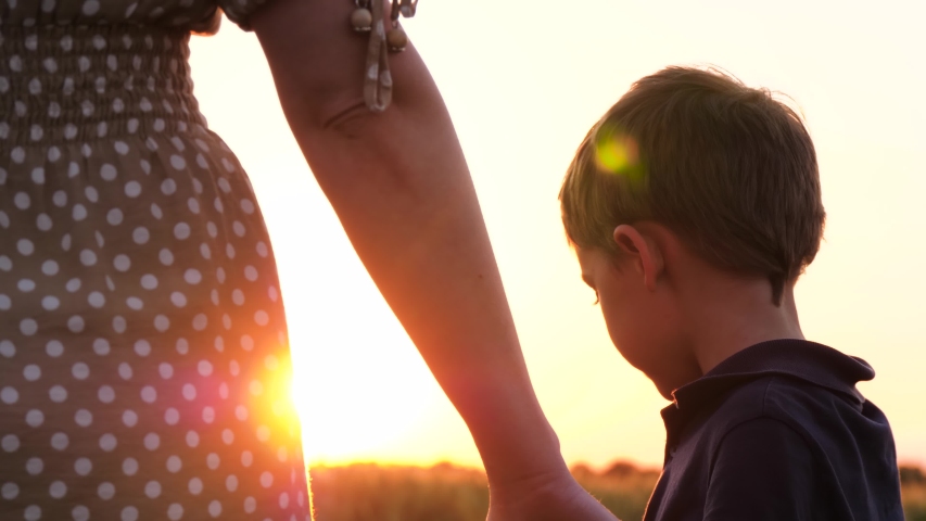 Mother walks with her son holding hands at sunset. A cute little child holds his mother's hand and looks at her experiencing emotions of happiness, a smile. The concept of a happy family and family Royalty-Free Stock Footage #1054724804