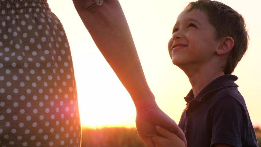 Mother walks with her son holding hands at sunset. A cute little child holds his mother's hand and looks at her experiencing emotions of happiness, a smile. The concept of a happy family and family | Shutterstock HD Video #1054724804