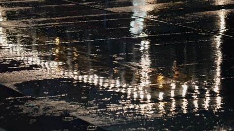 Rain drops at night, city lights abstract reflection in water on wet surface of concrete sidewalk