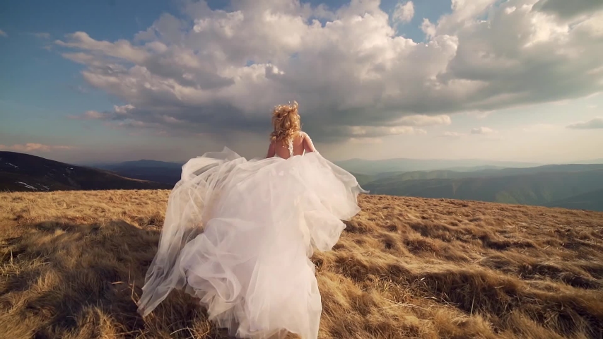 attractive young bride with white hair in a wedding dress walks or runs on the mountain, ha background of mountains and rocks landscape, dramatic sky. slow motion