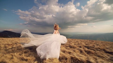 attractive young bride with white hair in a wedding dress walks or runs on the mountain, ha background of mountains and rocks landscape, dramatic sky. slow motion