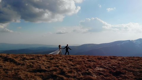 silhouette of the bride goes to the groom, the wedding couple runs up to each other, on top of the mountain, with landscapes of amazing nature. Blue sky and rocks, aerial view