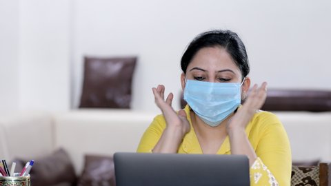 Sick Indian woman in a surgical mask busy over a video call - lifestyle concept. Young female happily doing a video call to her family and friends during the Covid-19 pandemic time in India