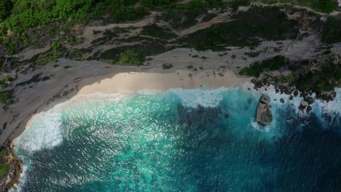 Top down aerial view of tropical beach with azure blue water and foaming ocean waves crashing on wild rocky beach. Shadow from the clouds moves slowly. Concept of nature