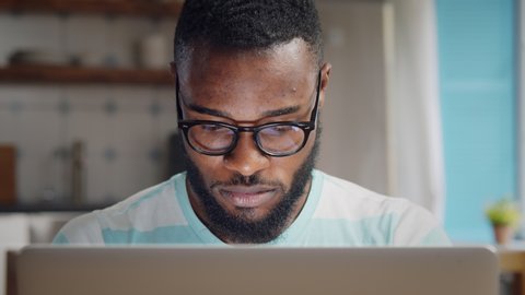 Young african freelancer man working on computer at home. Casual concentrated entrepreneur developing new project while working on laptop at home.