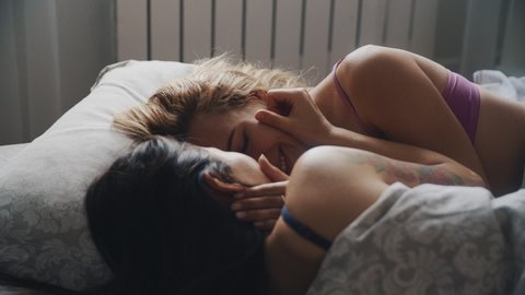 Multiethnic lesbian couple lie on bed, looking each other eyes. ITwo women sharing love and support. ntimate moment. LGBTQI, Pride Event, LGBT Pride Month, friendship concept. Gay family.