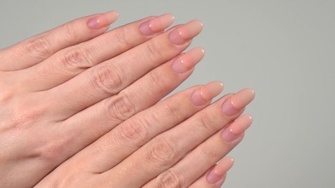 Closeup view video footage of two female hands with old worn long lasting painted nails with pink pastel gel polish cover. Woman shows regrowth of her nails.