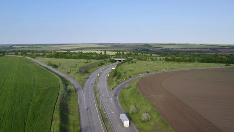 Aerial view on highway road through green fields on a summer sunny day. 4k footage of landscape with asphalt freeway between meadow and rural field. Drone shoots video of the countryside.