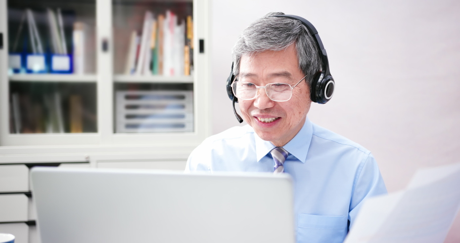 telework concept - Asian senior businessman use computer and headphone microphone to join a video meeting in the office