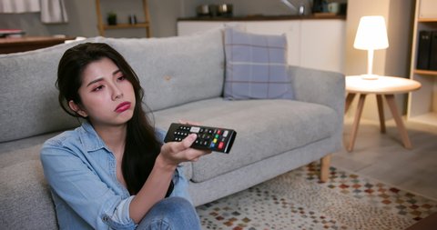 asian young woman is watching tv and feel bored sitting on the floor in living room at home