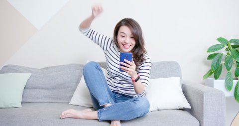 asian woman play mobile games and excited about her victory with fist gesture at home