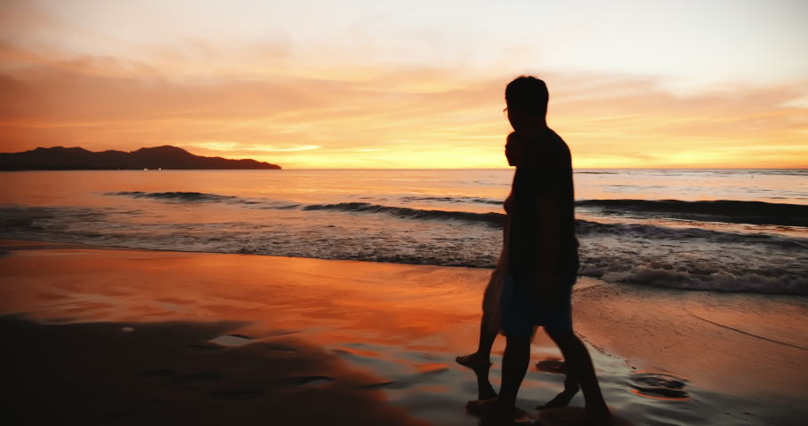 silhouette of asian couple holding each other hands and walking on the beach during sunset