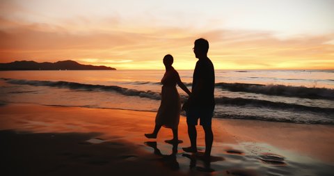 silhouette of asian couple holding each other hands and walking on the beach during sunset