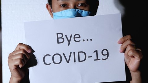 Light shining on Asian woman holding a paper labeled Bye COVID 19, stand on white background. Concept of say goodbye for Corona virus pandemic.