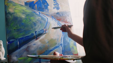 Young artist is working in his inspiring home studio, creating a new artwork, using bright acrylic paints, preferring contrast colors, enjoying the process of painting, Slow motion.