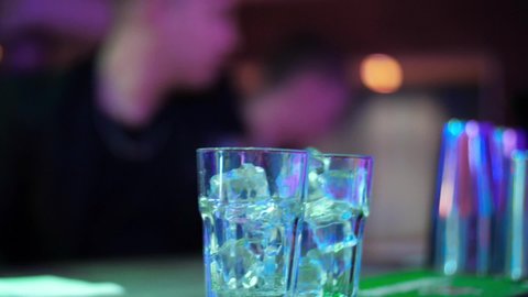Bartender pouring transparent alcoholic drink  from a bottle into shot glasses. Closeup. Set of several glasses with cocktails. Barman pouring drinks into glasses for drinking. 