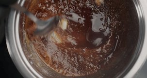 Tabletop slow motion video: confectioner in black gloves adds butter to the boiling melted sugar, chef makes hot caramel, cooking filling for cake, 4k 60fps Prores HQ 10 bit