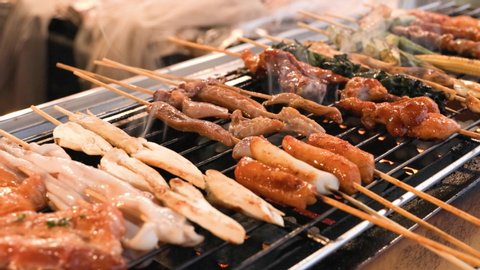 A street vendor is grilling assorted BBQ meat and vegetable on bamboo skewers with sauce. Street food snack selling at traditional market in Chiang Mai, Thailand.